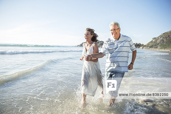 Older couple playing in waves on beach