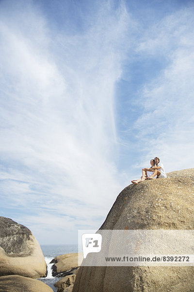 Couple sitting on rock formation on beach