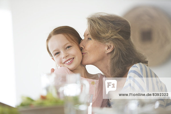 Ältere Frau küsst Enkelin bei Tisch