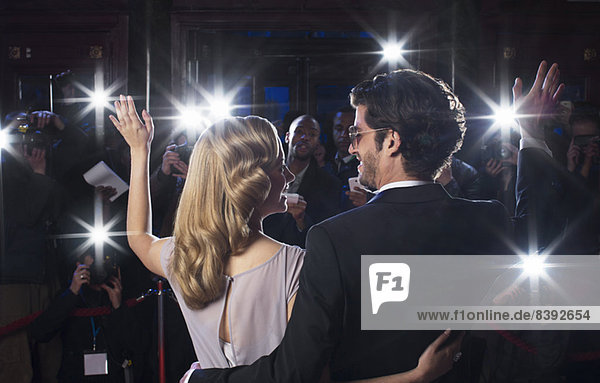 Rückansicht des Promi-Paares  das Paparazzi beim Red Carpet Event zuwinkt.