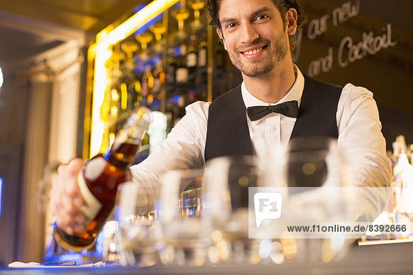 Porträt eines gut gekleideten Barkeepers  der Bourbon in eine Luxusbar gießt.