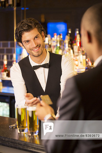 Gut gekleideter Barkeeper  der die Kreditkarte vom Kunden in der Luxusbar nimmt