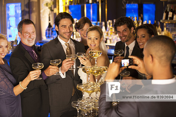 Man photographing bride and groom with friends at champagne pyramid