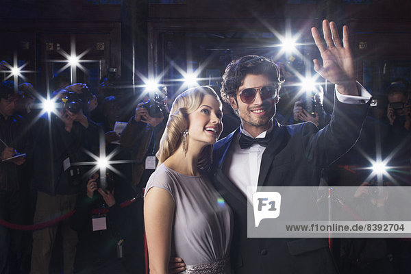 Well dressed celebrity couple waving to paparazzi at red carpet event