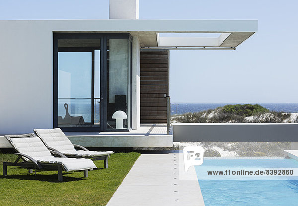 Liegestühle und Pool vor dem modernen Haus mit Blick auf den Ozean