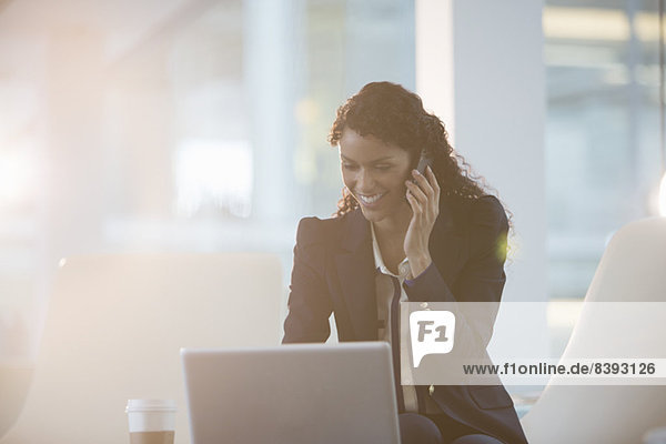 Businesswoman using laptop and cell phone in office