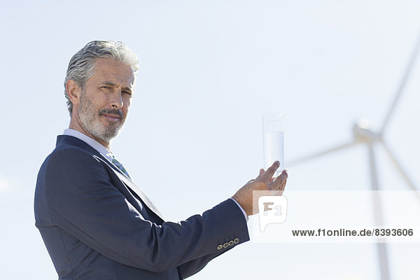 Geschäftsmann mit Glas Wasser durch Windkraftanlage