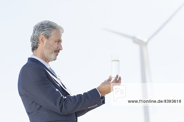 Geschäftsmann untersucht Wasserglas mit Windkraftanlage