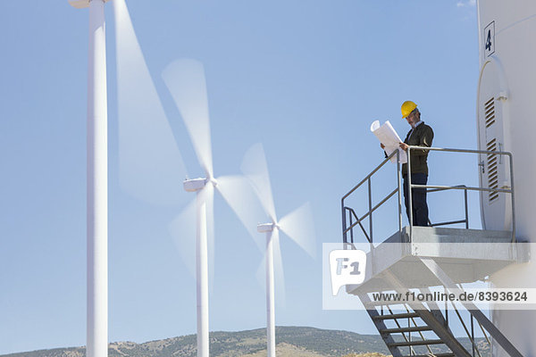 Geschäftsmann untersucht Blaupausen von Windkraftanlagen in ländlicher Landschaft