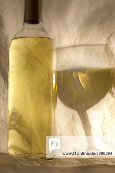 Weißweinflasche und Reflexion von Weinglas auf Seidenpapier
