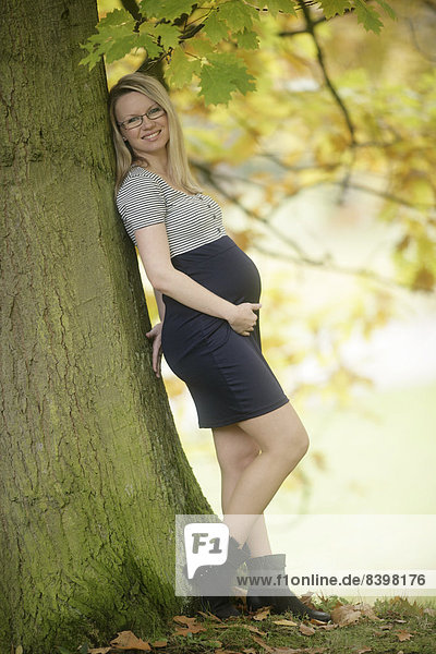 Schwangere Frau  28 Jahre  lehnt an Baum