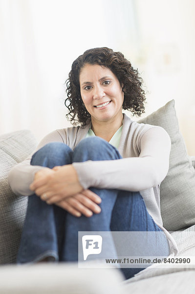 Hispanic woman hugging her knees on sofa