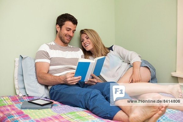 Couple relaxing on bed looking at book