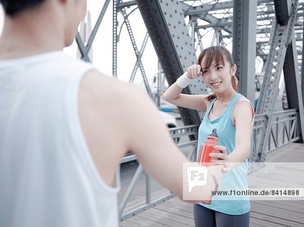 Männlicher Jogger übergibt Wasserflasche an weibliche Begleiterin