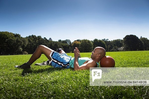 Young man lying on grass with head on basketball