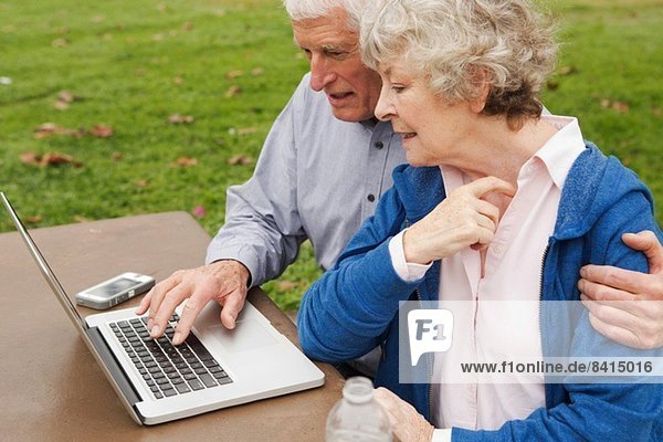Ehemann und Ehefrau lernen den Umgang mit dem Laptop im Park