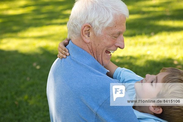Großvater kniend auf Gras umarmendem Enkel