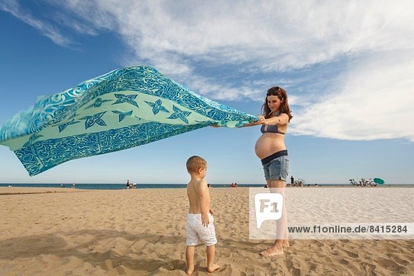 Schwangere Frau am Strand mit Decke  die im Wind weht