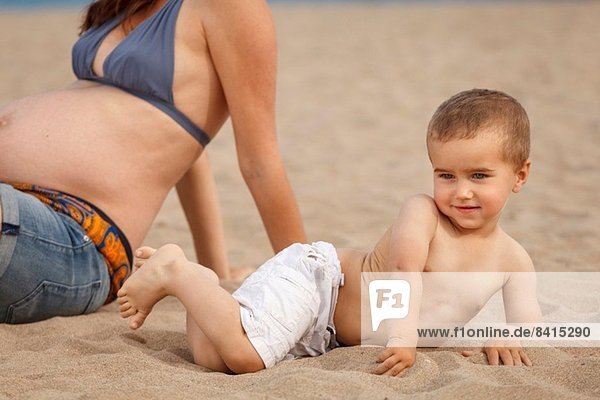 Abgeschnittenes Bild einer schwangeren Mutter und eines schwangeren Sohnes am Strand.