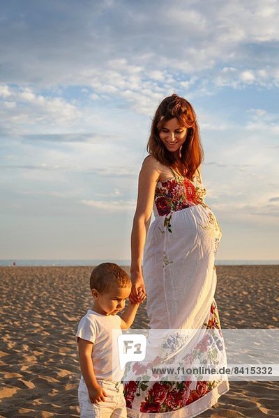 Mutter und Kleinkind gehen am Strand entlang und halten Händchen.