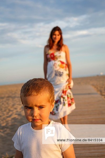 Toddler standing on boardwalk  mother in background