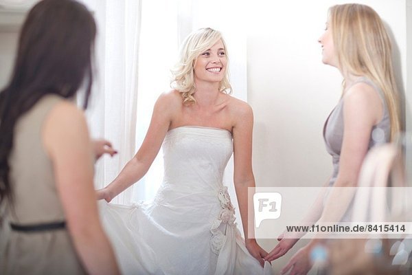 Junge Frau beim Anprobieren des Brautkleides  mit Freunden