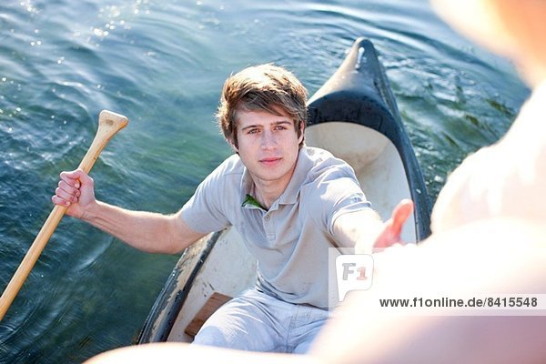 Young man in rowing boat reaching up to female friends