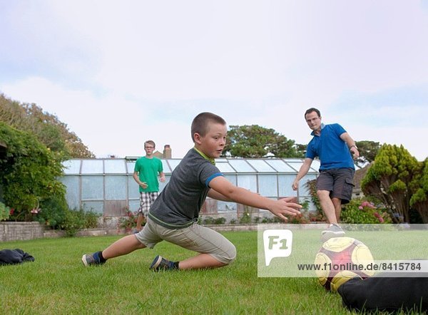 Vater und Söhne spielen Fußball im Garten