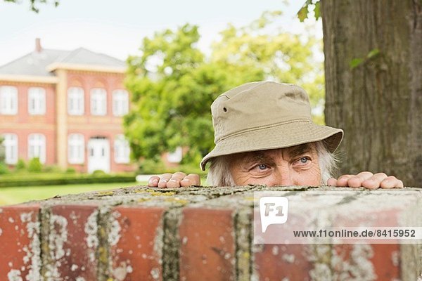 Älterer Mann mit Hut und Blick über die Gartenmauer