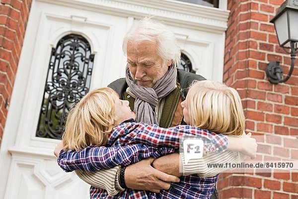 Großvater umarmt Enkelkinder vor der Haustür