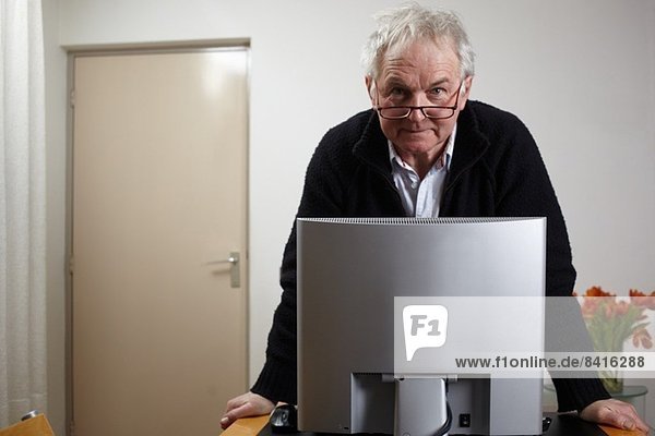 Senior-Mann zu Hause vor dem Personal-Computer stehend