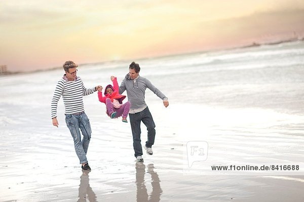 Gay couple swinging child on beach