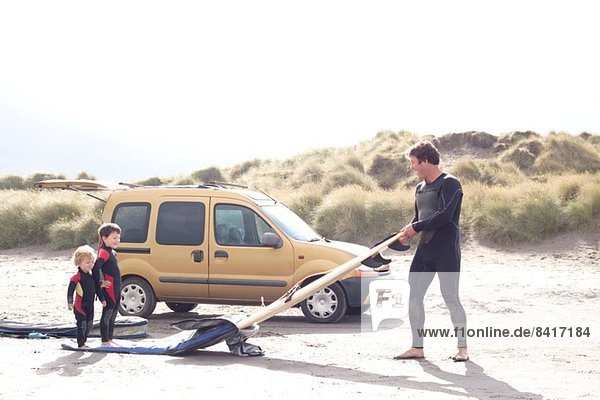 Vater mit zwei Söhnen  Surfbrett und Auto am Strand