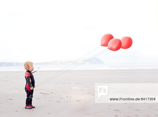Portrait des Jungen am Strand mit roten Luftballons