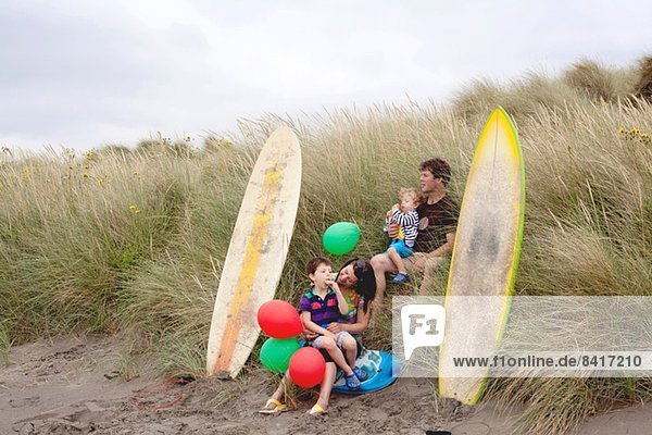 Familie mit zwei Jungen am Strand mit Surfbrettern