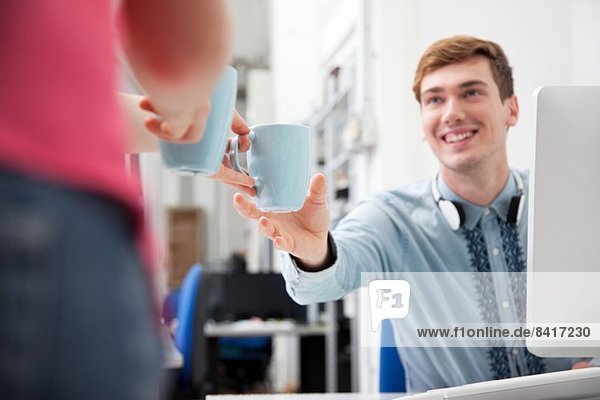 Frau gibt jungen Mann Kaffee im Büro