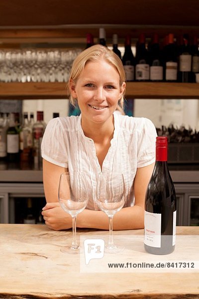 Portrait der Kellnerin mit Weinflasche und Gläsern an der Küchentheke