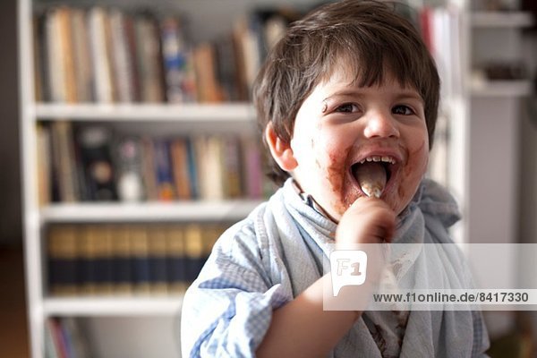 Portrait of male toddler licking chocolate covered teaspoon