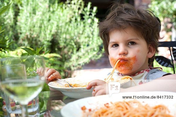 Porträt eines unordentlichen männlichen Kleinkindes  das Spaghetti isst.