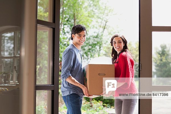 Young couple carrying cardboard box into new house