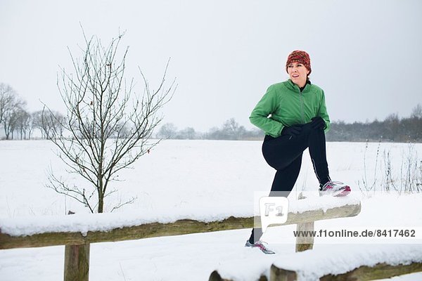 Weibliche Joggerin  die sich vor dem Lauf in einer schneebedeckten Szene ausdehnt.