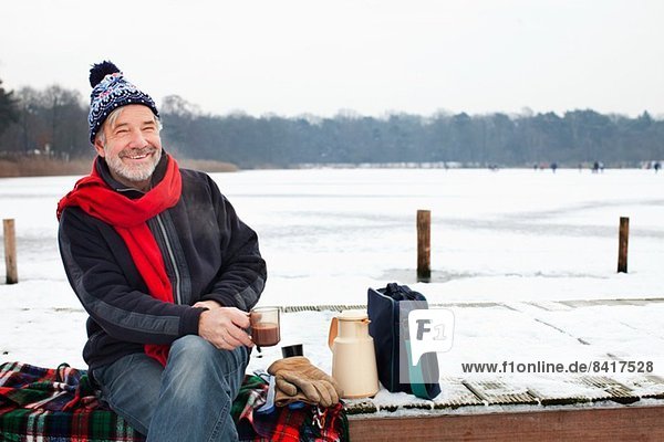 Man sitting on pier having hot drink