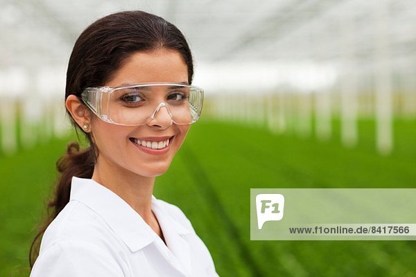 Wissenschaftler mit Schutzbrille vor Pflanzen im Gewächshaus