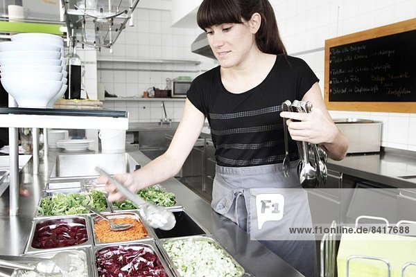 Frau  die in der Restaurantküche arbeitet und eine Salatzange hält