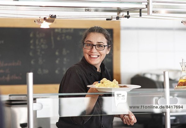Frau  die in der Restaurantküche arbeitet und Mahlzeiten serviert