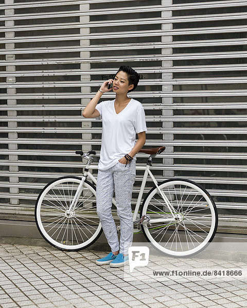 Young woman leaning against bicycle using smartphone