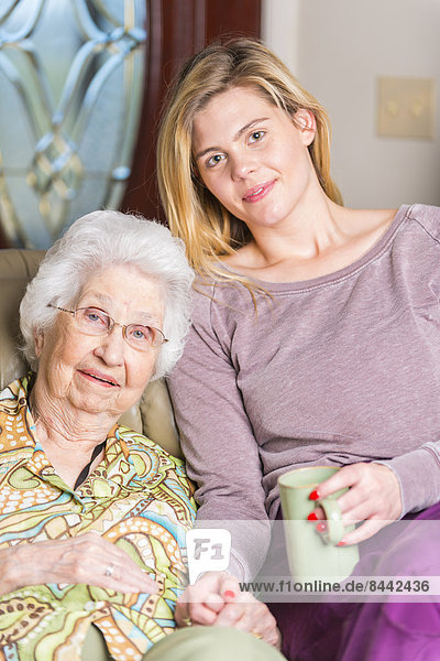 Aged woman and her great-granddaughter sitting side by side