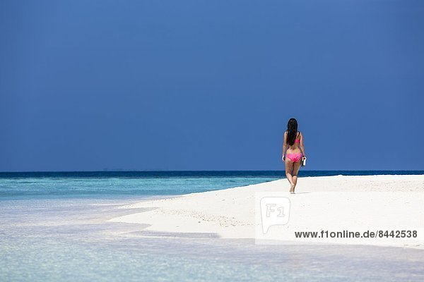 Malediven  Junge Frau im Bikini am Strand spazieren gehen