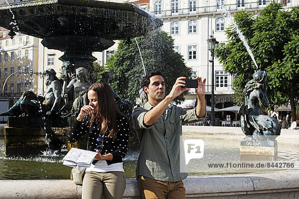 Portugal  Lisboa  Baixa  Rossio  Praca Dom Pedro IV  young couple with city map and smart phone in front of a fountain