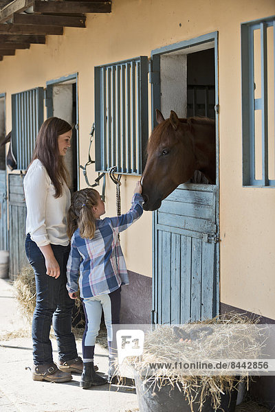 Frau und Mädchen streichelndes Pferd im Stall